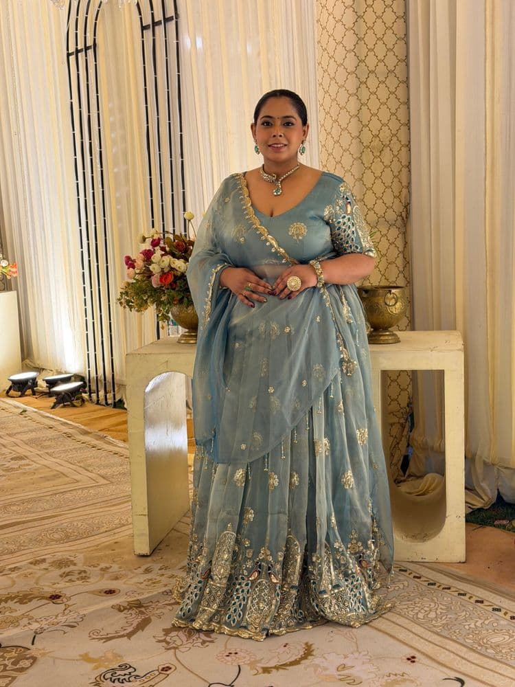 Woman in a sage blue-grey lehenga with a peacock-motif blouse.