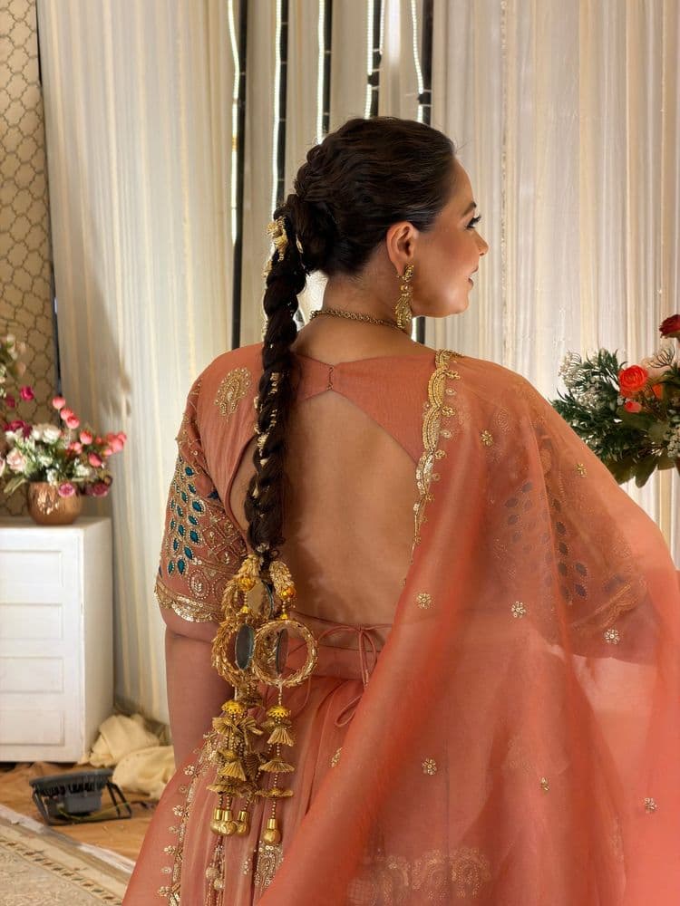 Two models in peach and coral organza lehengas with mirror-work hems and peacock-sleeve blouses.
